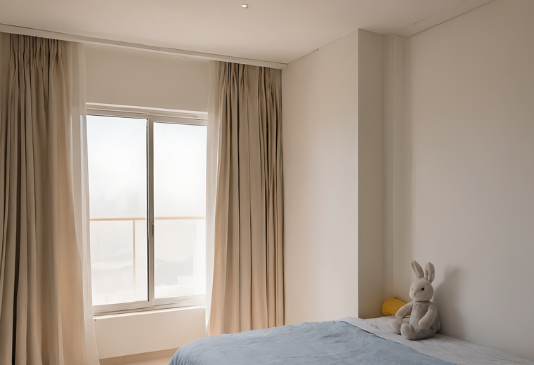 Child's bedroom in a Dubai apartment with a closed window, long beige curtains and a soft toy on the bed